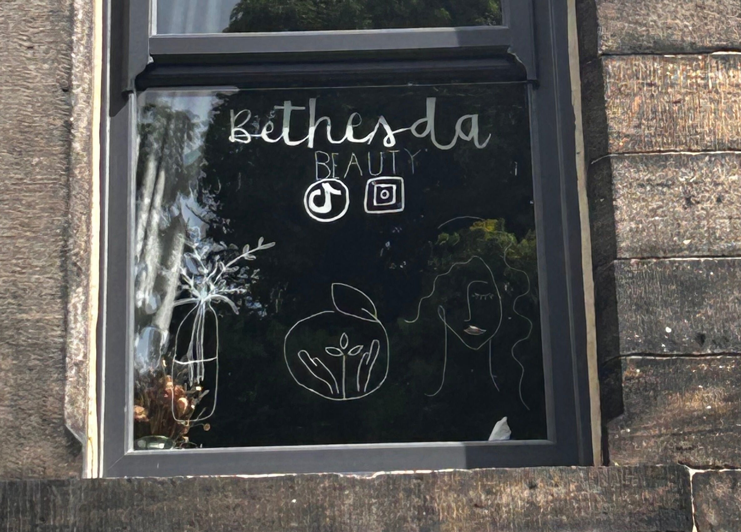 Window display at Bethesda Beauty, Rawdon, England, GB showcasing artistic designs and logo.
