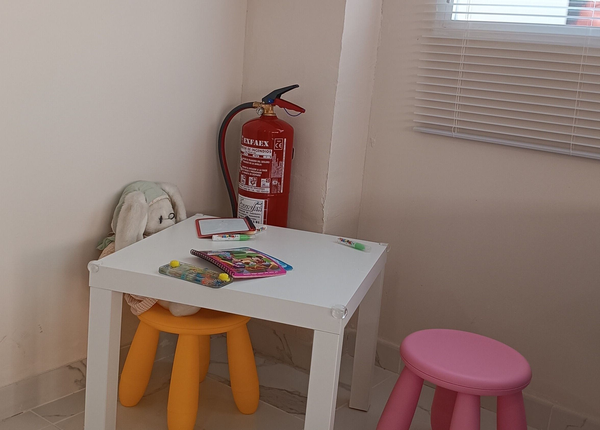 Zona infantil en Glowy Beauty Salon, Sagunt, Comunidad Valenciana, ES, con mesa blanca y taburetes coloridos.