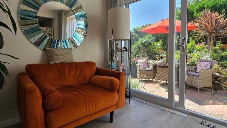Cozy seating at Fern Wellbeing, Paignton, England. Bright couch, mirror, and garden view enhance relaxation space.