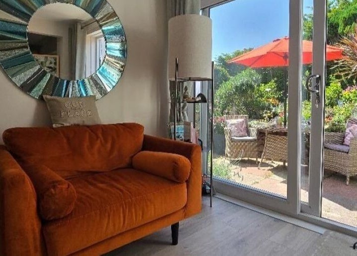 Cozy seating at Fern Wellbeing, Paignton, England. Bright couch, mirror, and garden view enhance relaxation space.