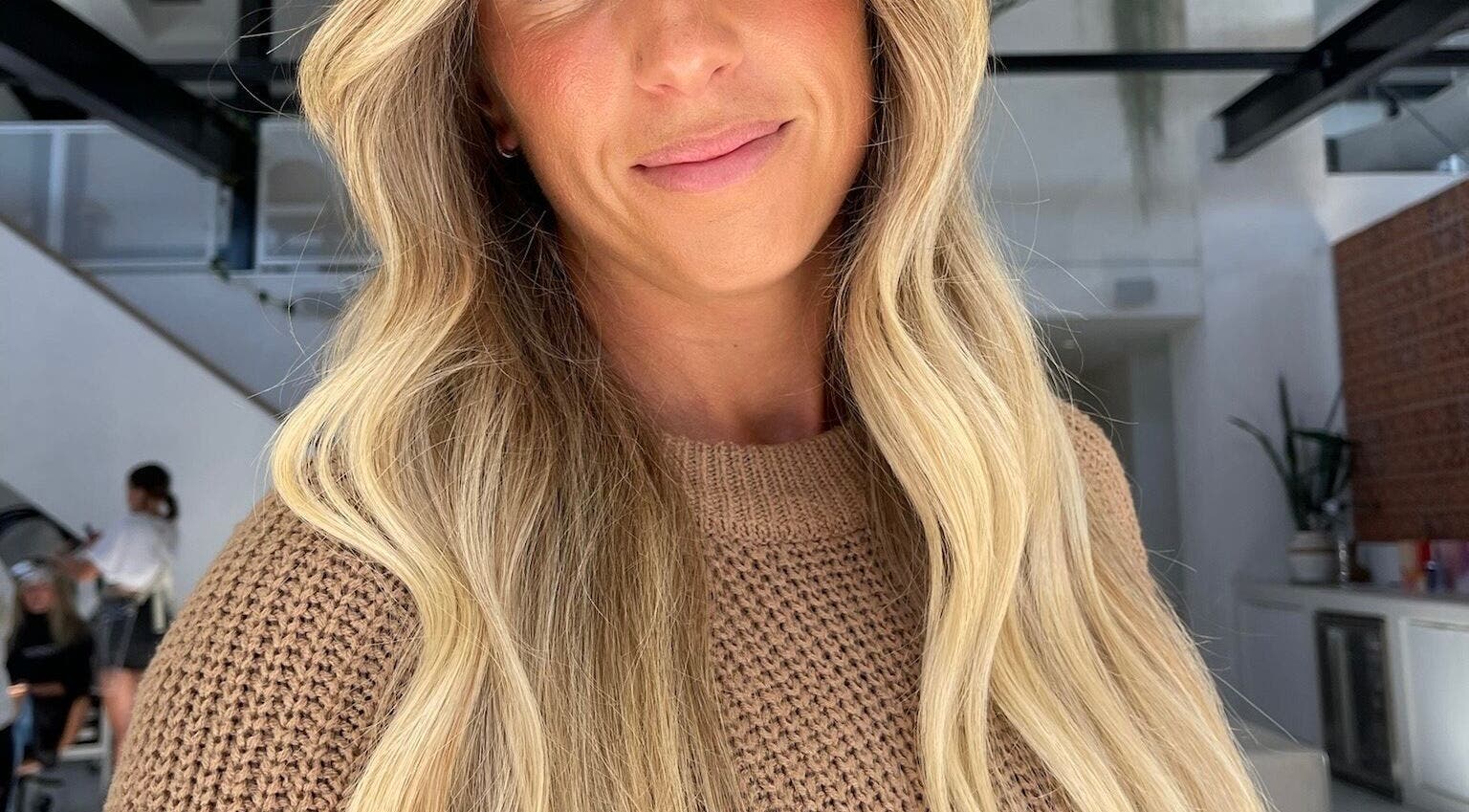 Woman with long, wavy blonde hair at VÉRAH, Yeppoon, Queensland, AU. Luxurious salon setting.