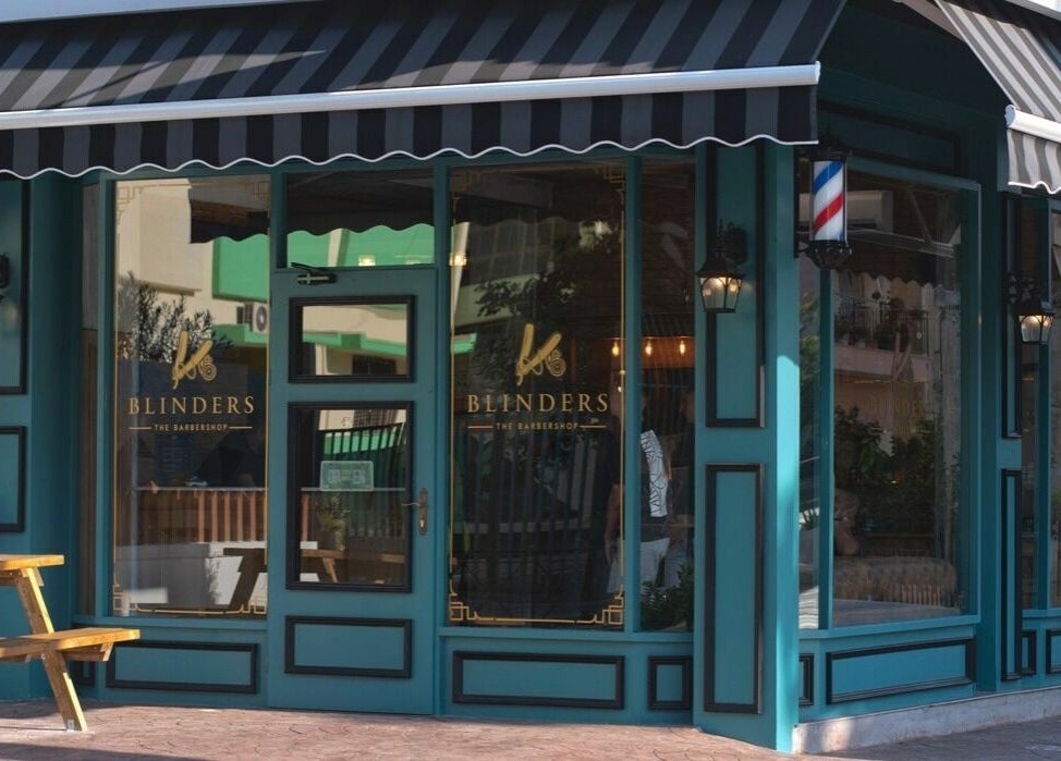 Εξωτερική όψη του Blinders Barbershop στην Αθήνα, GR με πράσινη πρόσοψη και ξύλινο καθιστικό.