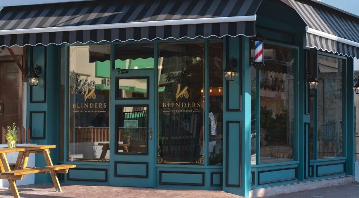 Εξωτερική όψη του Blinders Barbershop στην Αθήνα, GR με πράσινη πρόσοψη και ξύλινο καθιστικό.