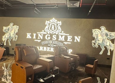 Luxurious interior of Kingsmen Barbershop, Dubai, with plush chairs and illuminated logo on the wall.