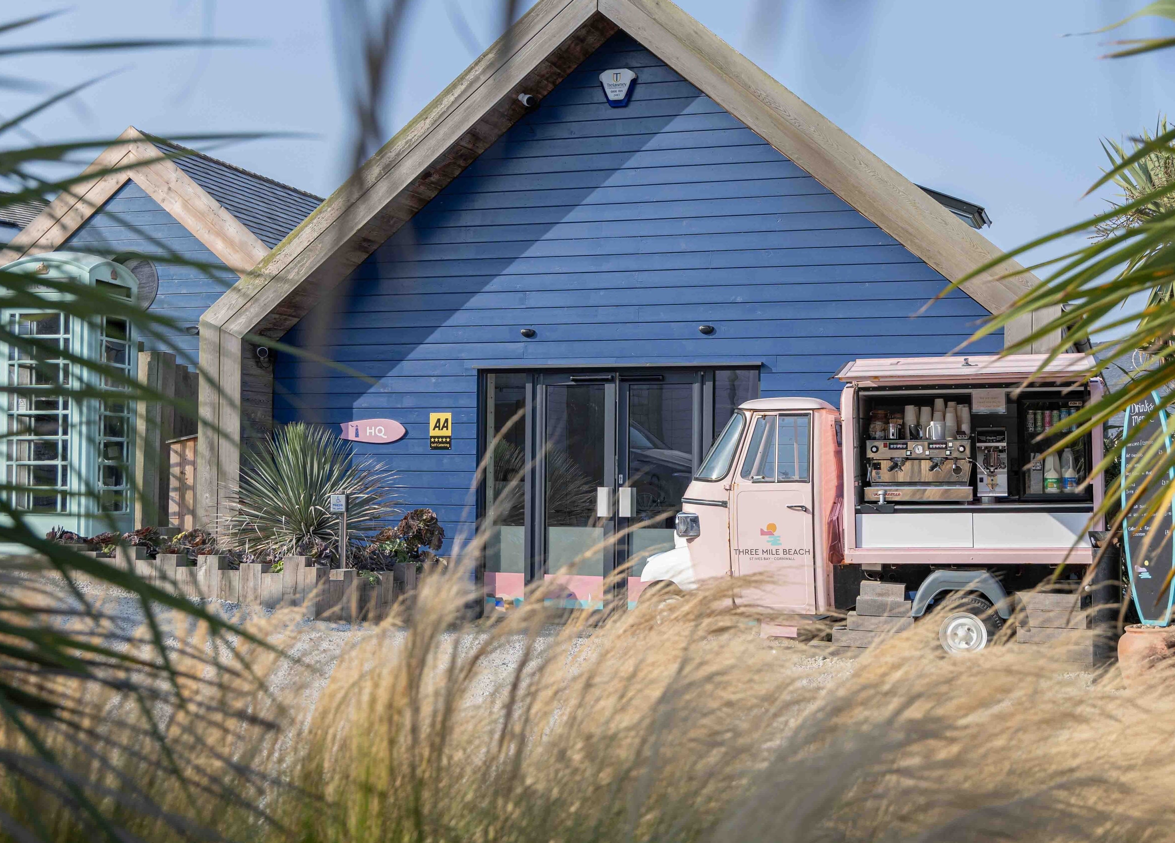 Relax at Three Mile Beach's vibrant blue cabin in Gwithian, England, GB, framed by lush greenery.