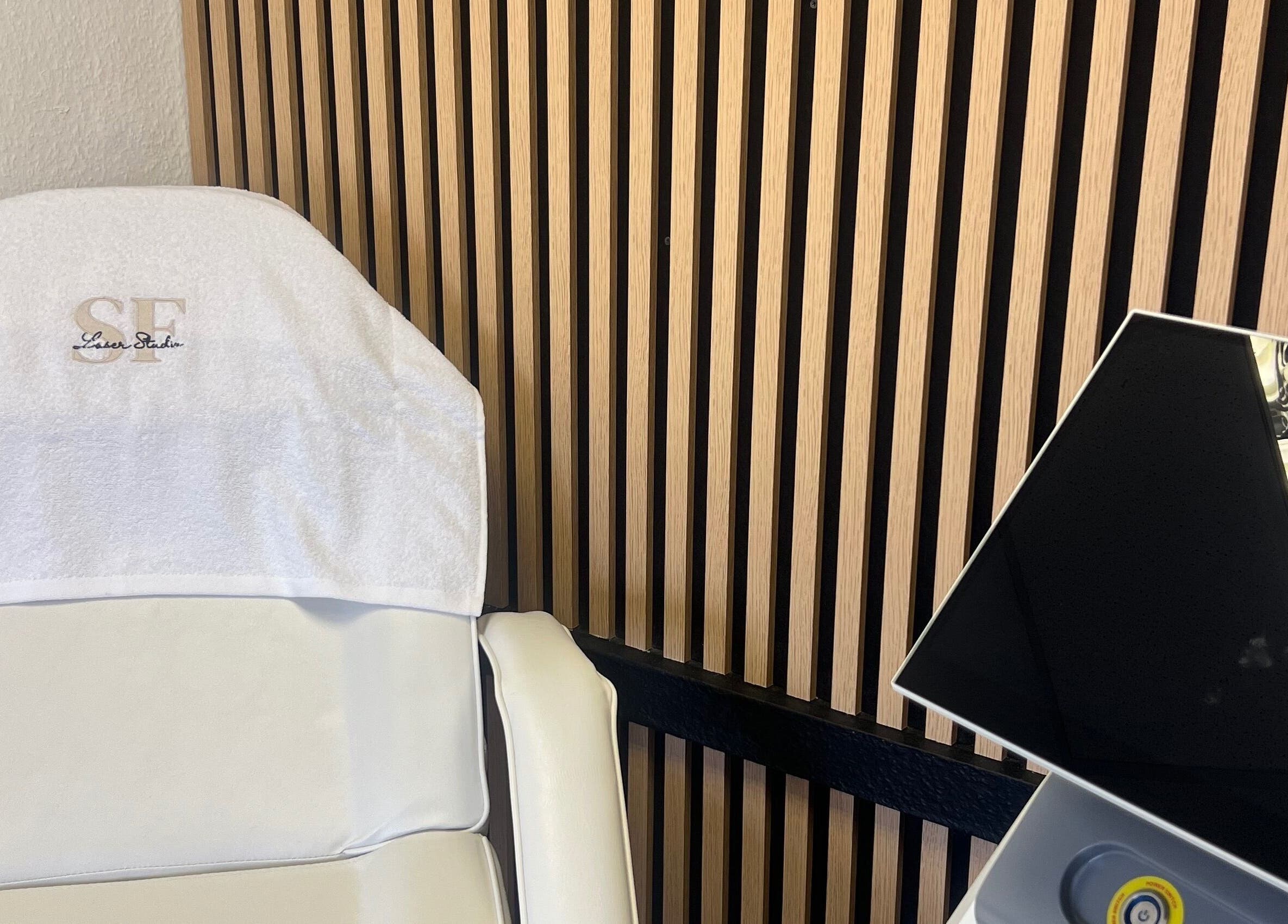 Modern treatment chair in SF LASER, Dereham, England, GB with striped wooden wall and sleek equipment.