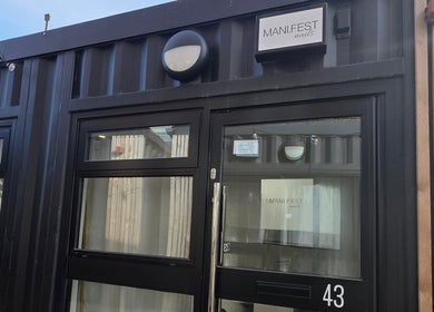 Entrance of MANI.FEST Nails salon in Barry, Wales, GB, showcasing modern black door and sign.