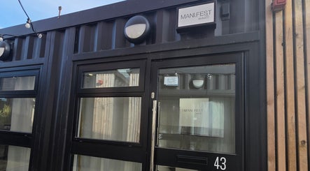 Entrance of MANI.FEST Nails salon in Barry, Wales, GB, showcasing modern black door and sign.