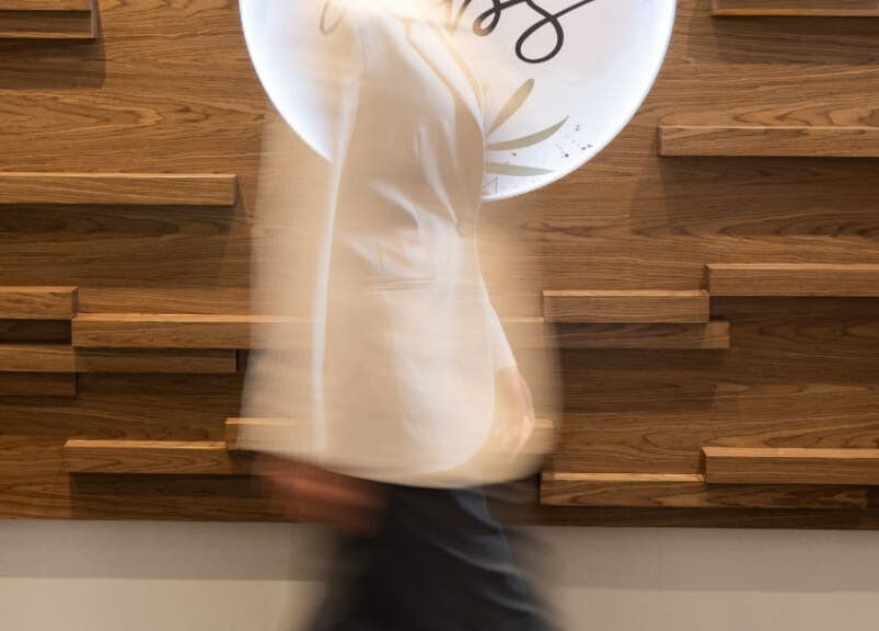 A person walking past the stylish wooden decor at MBS Nails Spa, Muscat, OM.