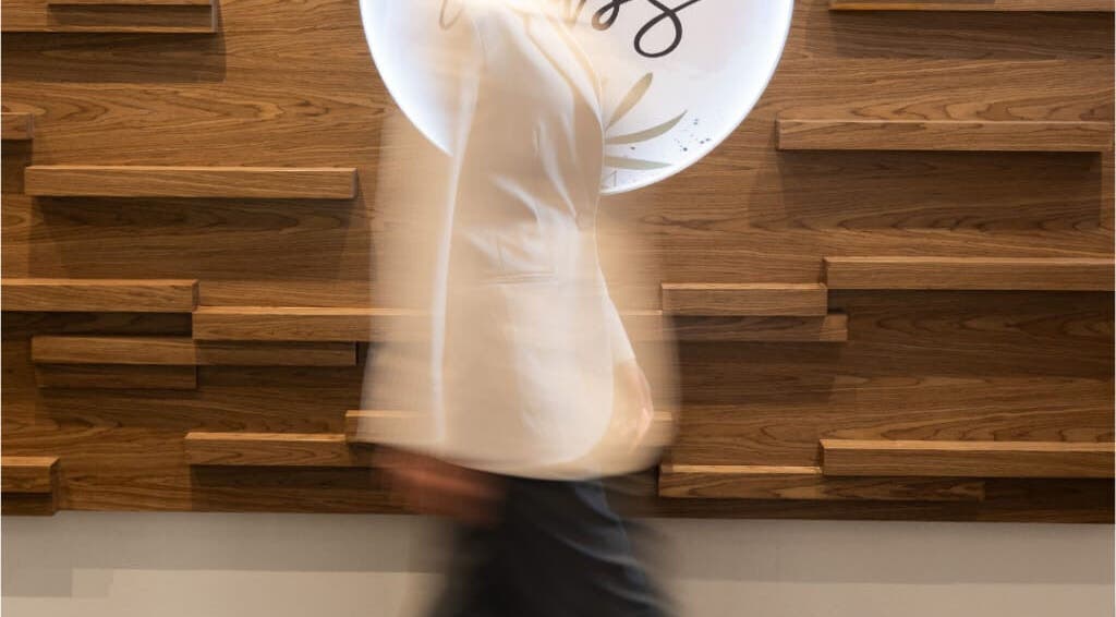 A person walking past the stylish wooden decor at MBS Nails Spa, Muscat, OM.