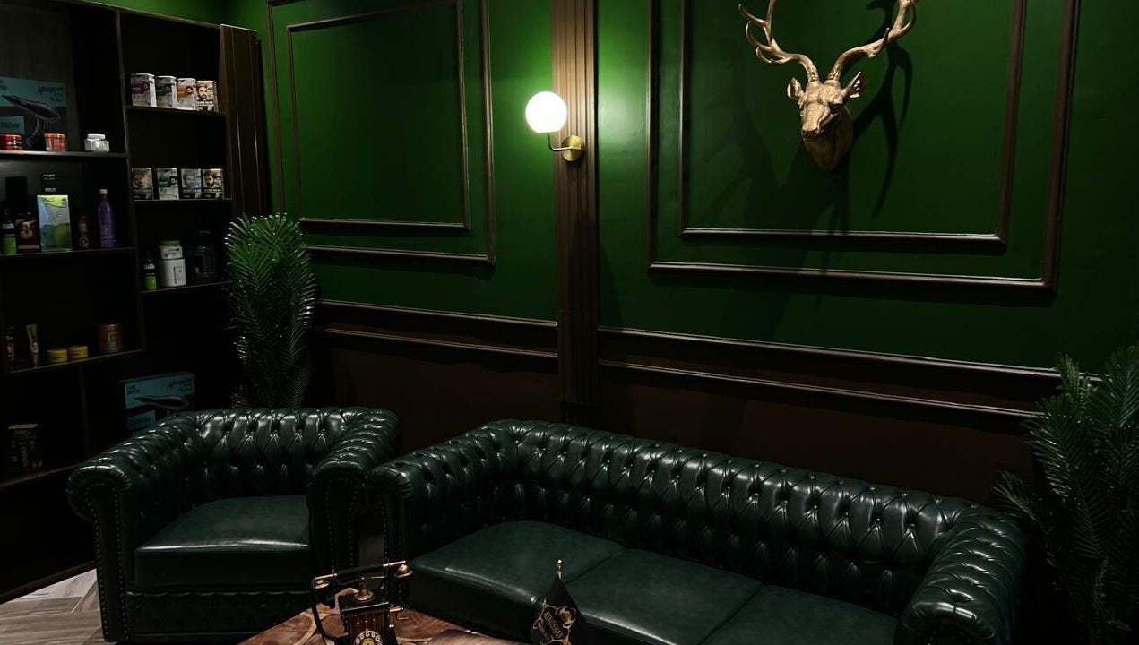 Elegant green interior of Kingsman Barbershop, Riyadh, Riyadh Province, SA with leather sofas and wall decor.