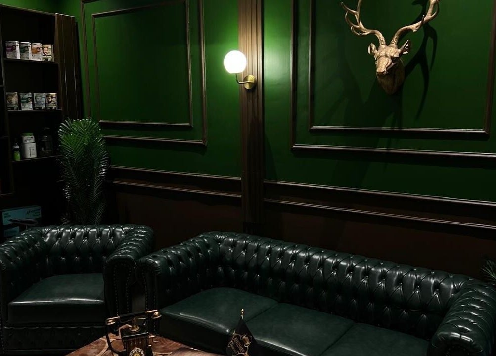 Elegant green interior of Kingsman Barbershop, Riyadh, Riyadh Province, SA with leather sofas and wall decor.