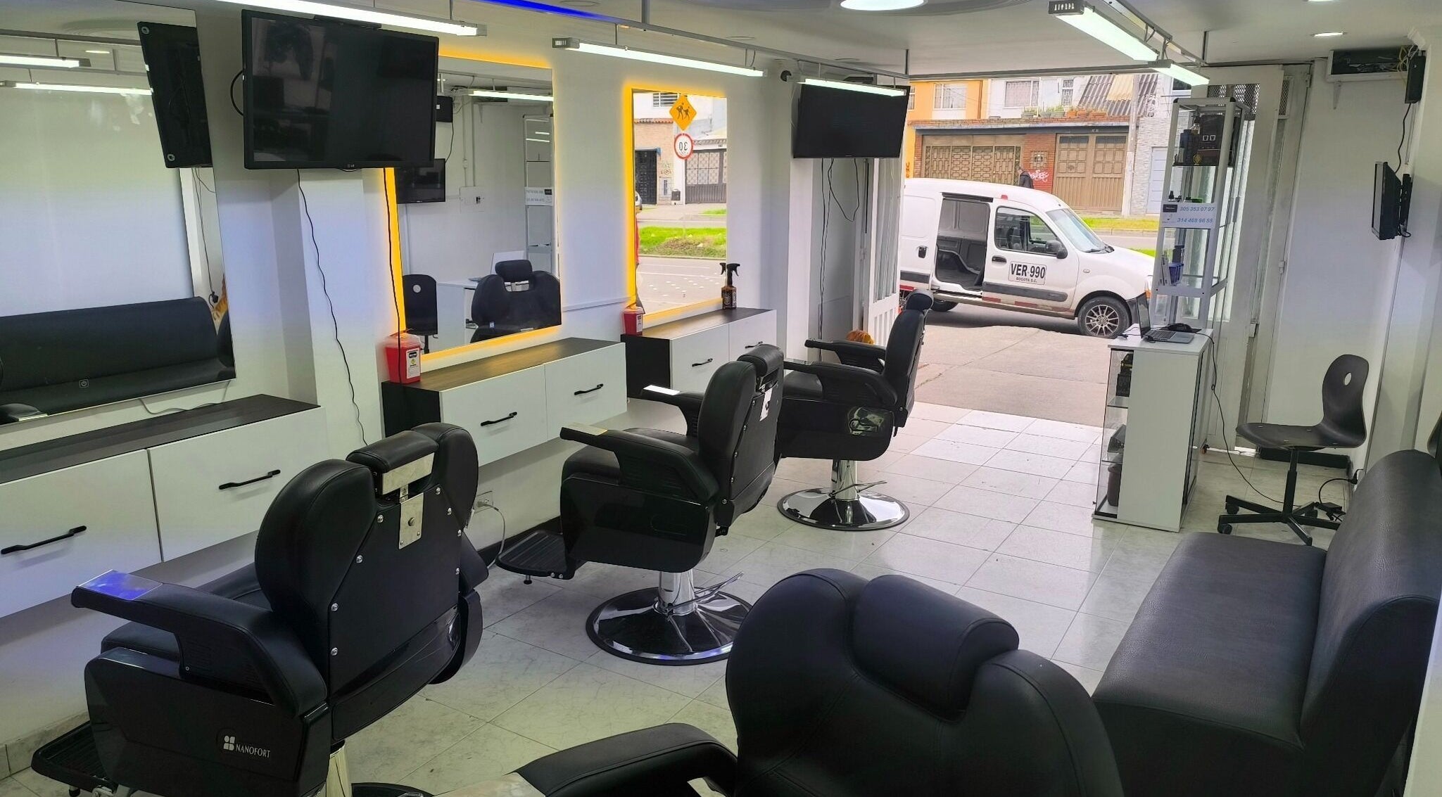 Interior moderno de Barbería LUXFADE en Bogotá, Bogotá, CO, mostrando sillas de barbería elegantes y espejos iluminados.