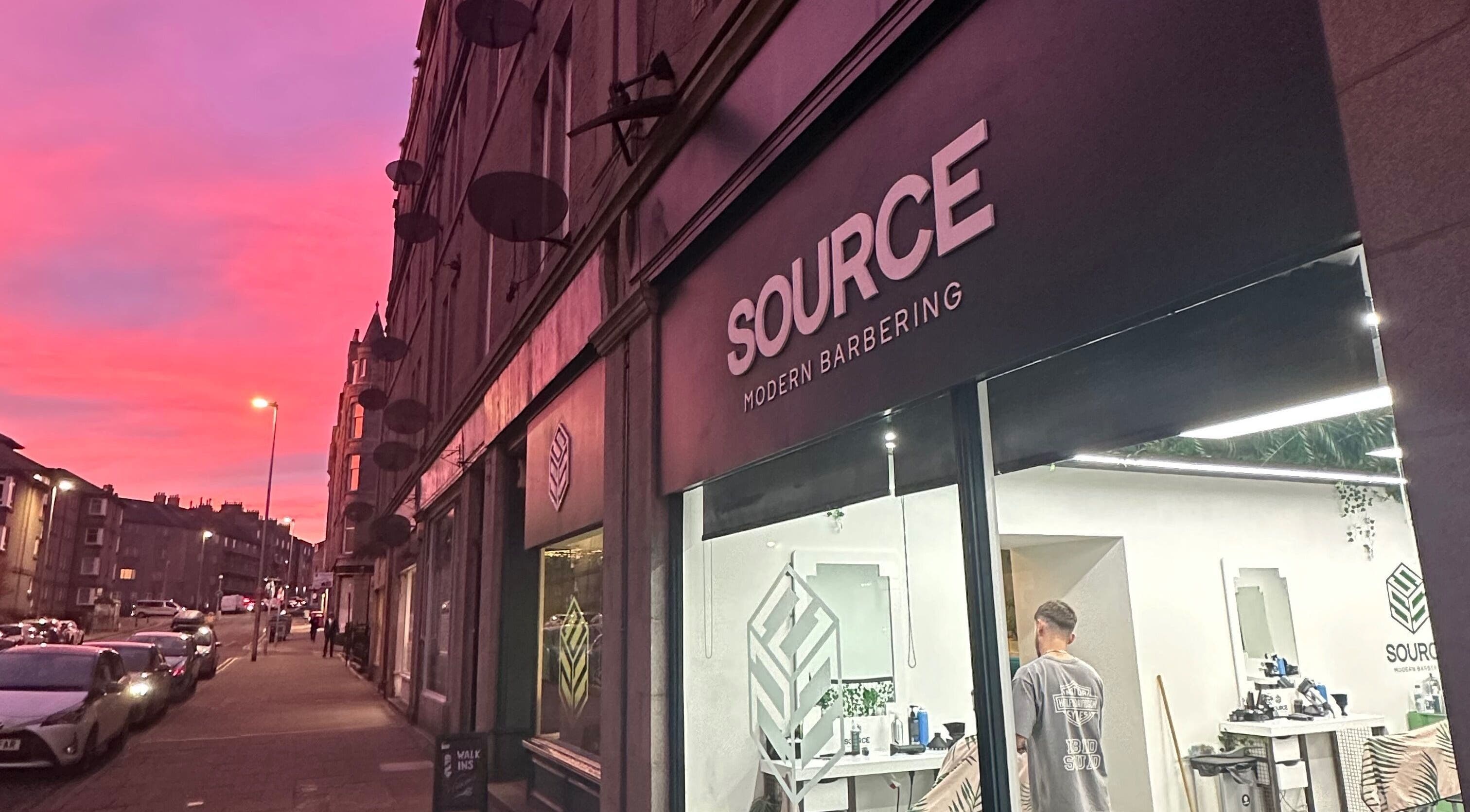 Source Barbers in Aberdeen, Scotland, GB at sunset with a vibrant pink sky and street view.