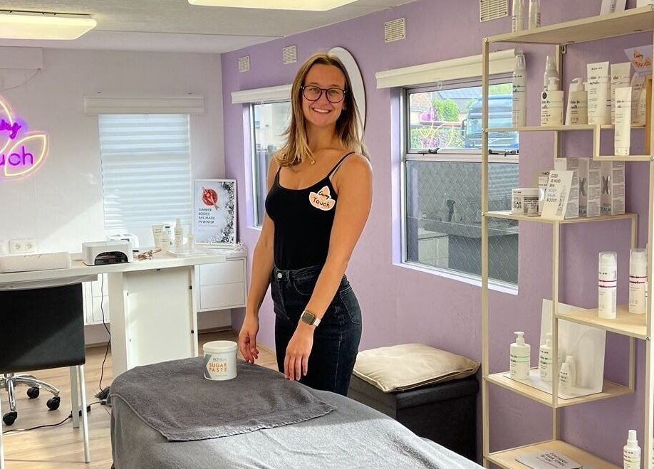 Vriendelijke medewerker bij Caring Touch, Tessenderlo-ham, Vlaanderen, BE, omringd door schoonheidsproducten.