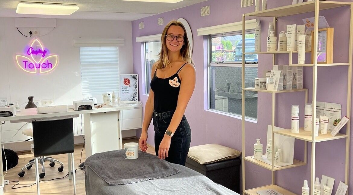 Vriendelijke medewerker bij Caring Touch, Tessenderlo-ham, Vlaanderen, BE, omringd door schoonheidsproducten.