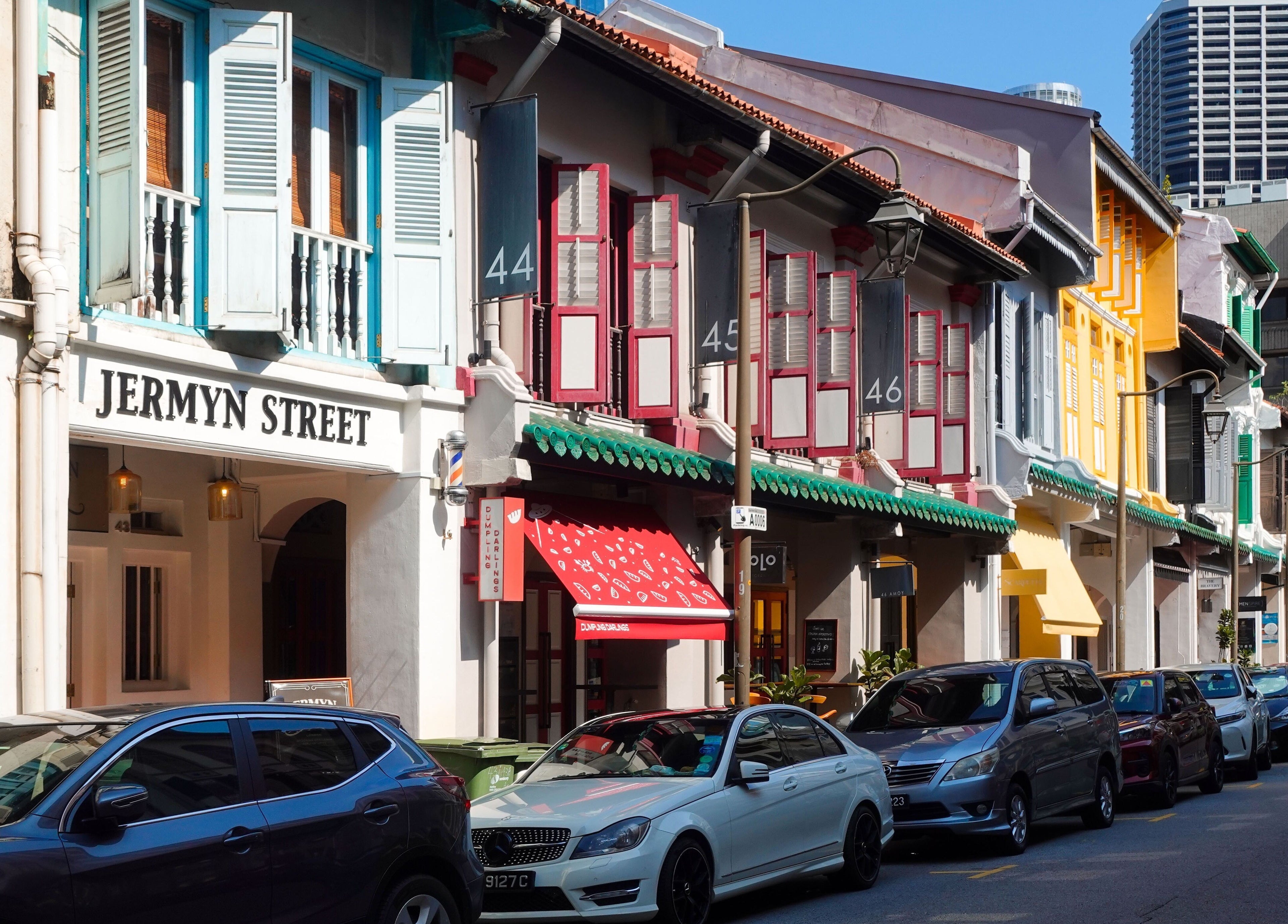 Colorful historic storefronts at Jermyn Street, Singapore, Singapore, SG with parked cars lining the street.