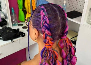 Colorful braided hairstyle at Braids To Go in Noord, AW. Vibrant purple, pink, and orange tones.
