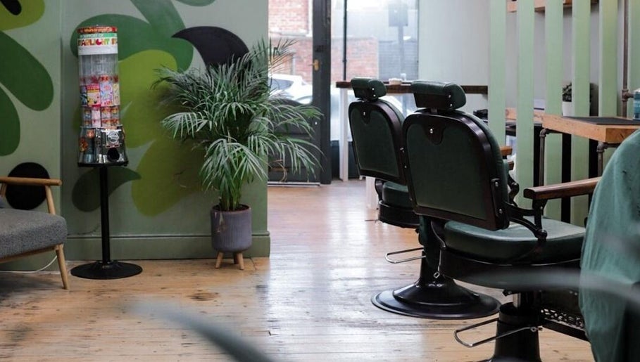 Stylish interior of Lishmans Barbershop in Newcastle upon Tyne, England, GB with green chairs and plant decor.