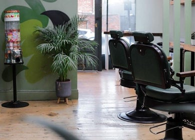 Stylish interior of Lishmans Barbershop in Newcastle upon Tyne, England, GB with green chairs and plant decor.