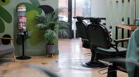 Stylish interior of Lishmans Barbershop in Newcastle upon Tyne, England, GB with green chairs and plant decor.