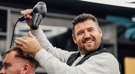 A barber at Lishmans Barbershop in Newcastle upon Tyne, England, styling a client's hair with a blow dryer.