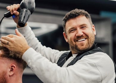 Barber styling hair at Lishmans Barbershop, Newcastle upon Tyne, England, GB with a wide smile.