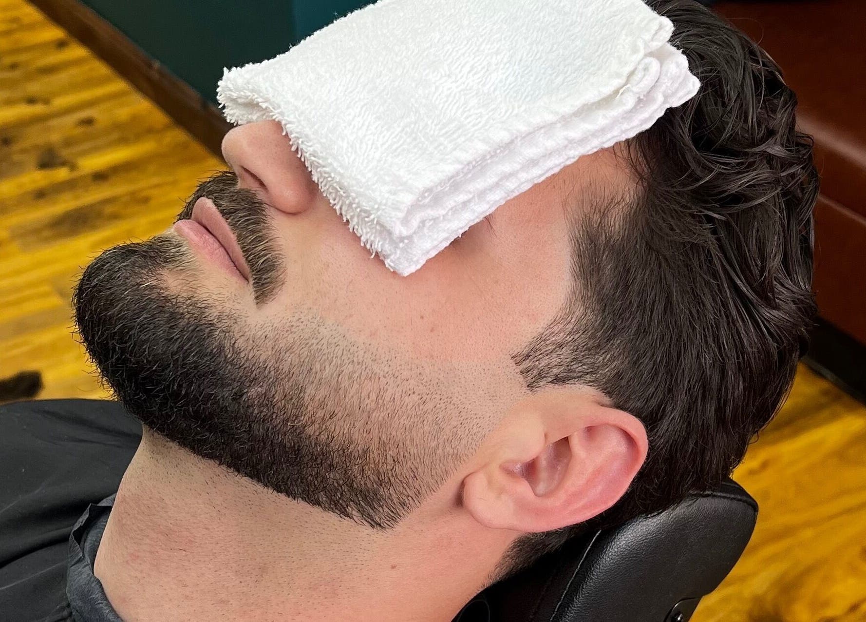 Man enjoying facial treatment at Fade Factory - Balham, London, England, GB with a hot towel on his face.