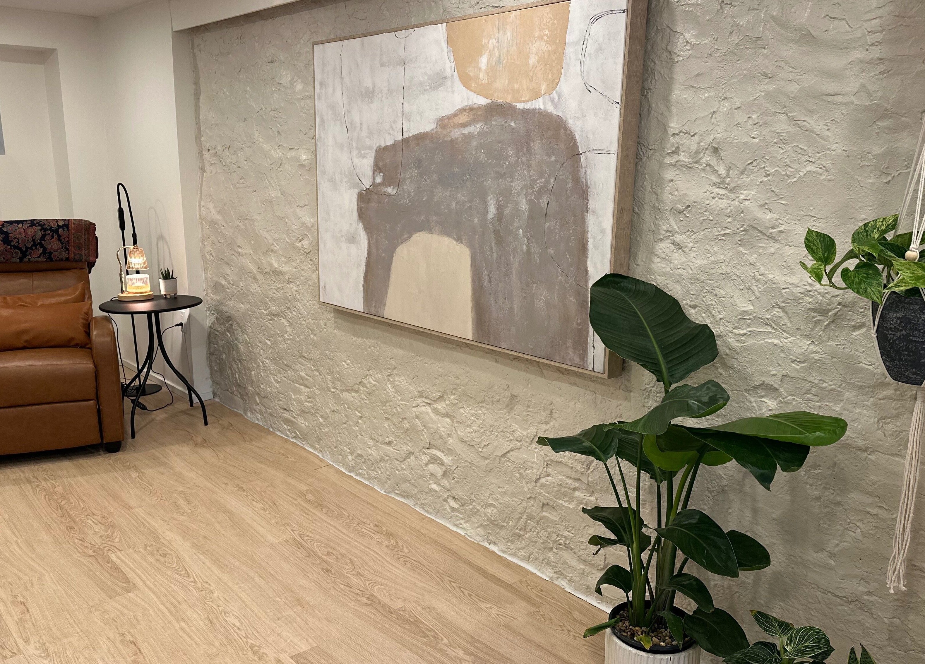 Studio Enu in Toronto, Ontario, CA features a cozy corner with a leather chair, abstract art, and lush plants.