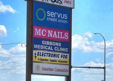 Sign featuring Mc Nails in Gibbons, Alberta, CA, alongside other local businesses under a blue sky.