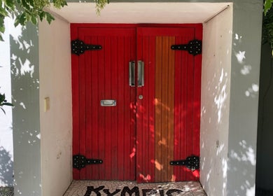 Red wooden door at Kymric Hall, Franschhoek, Western Cape, ZA, framed by green foliage.