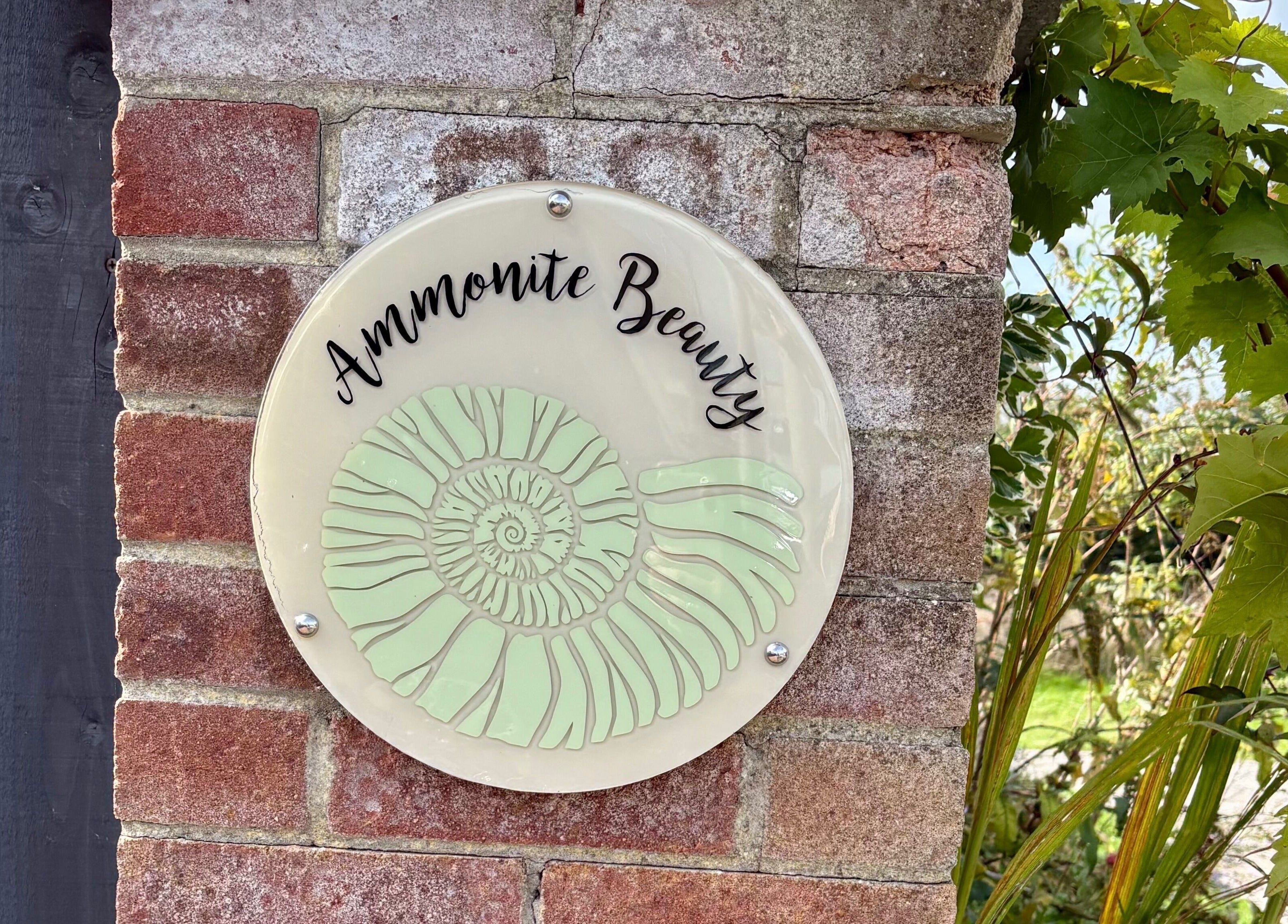 Ammonite Beauty sign on brick wall, Bridport, England, GB.