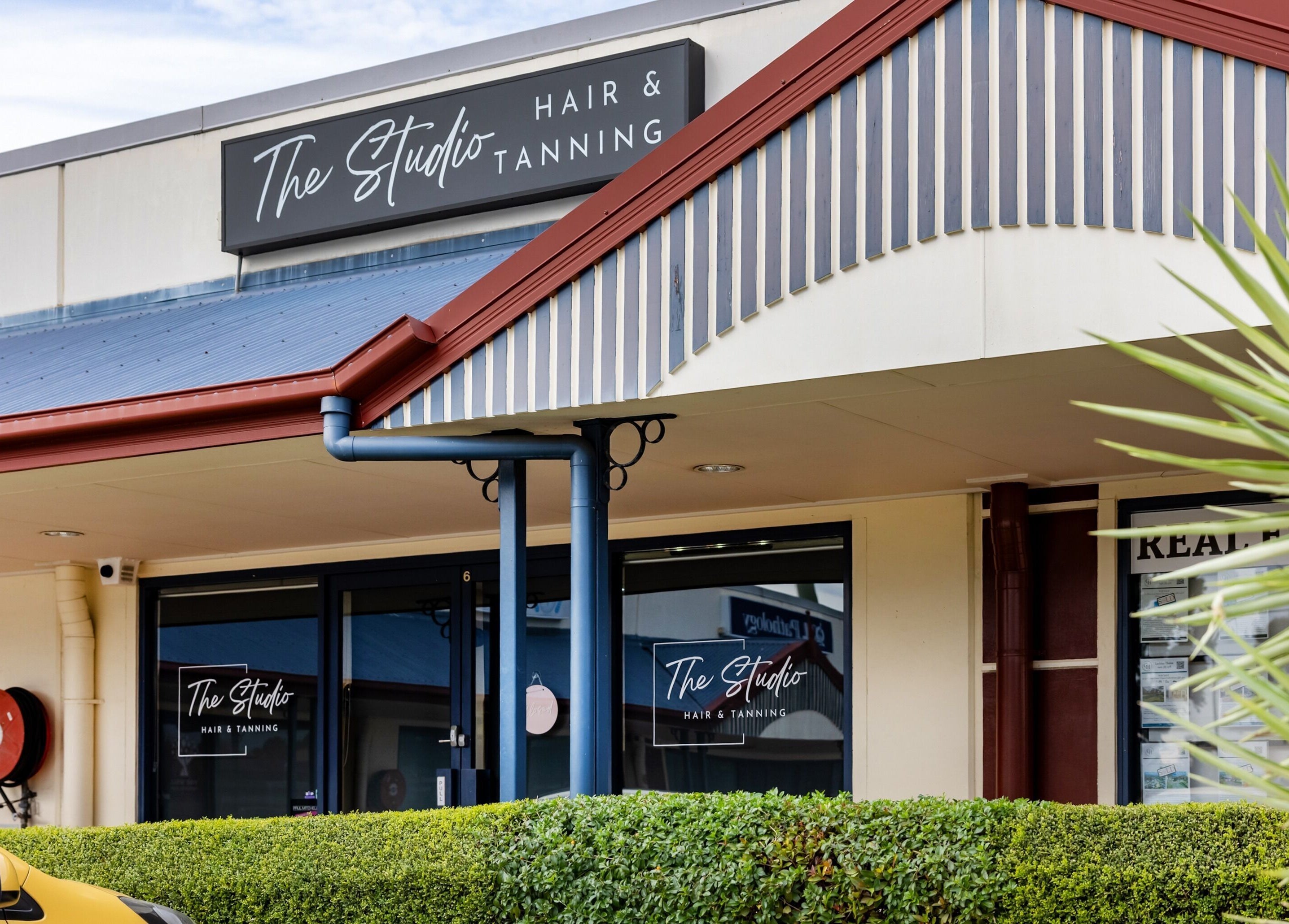 Front exterior of The Studio Hair & Tanning at Deception Bay, Queensland, AU, showing signage and lush hedges.