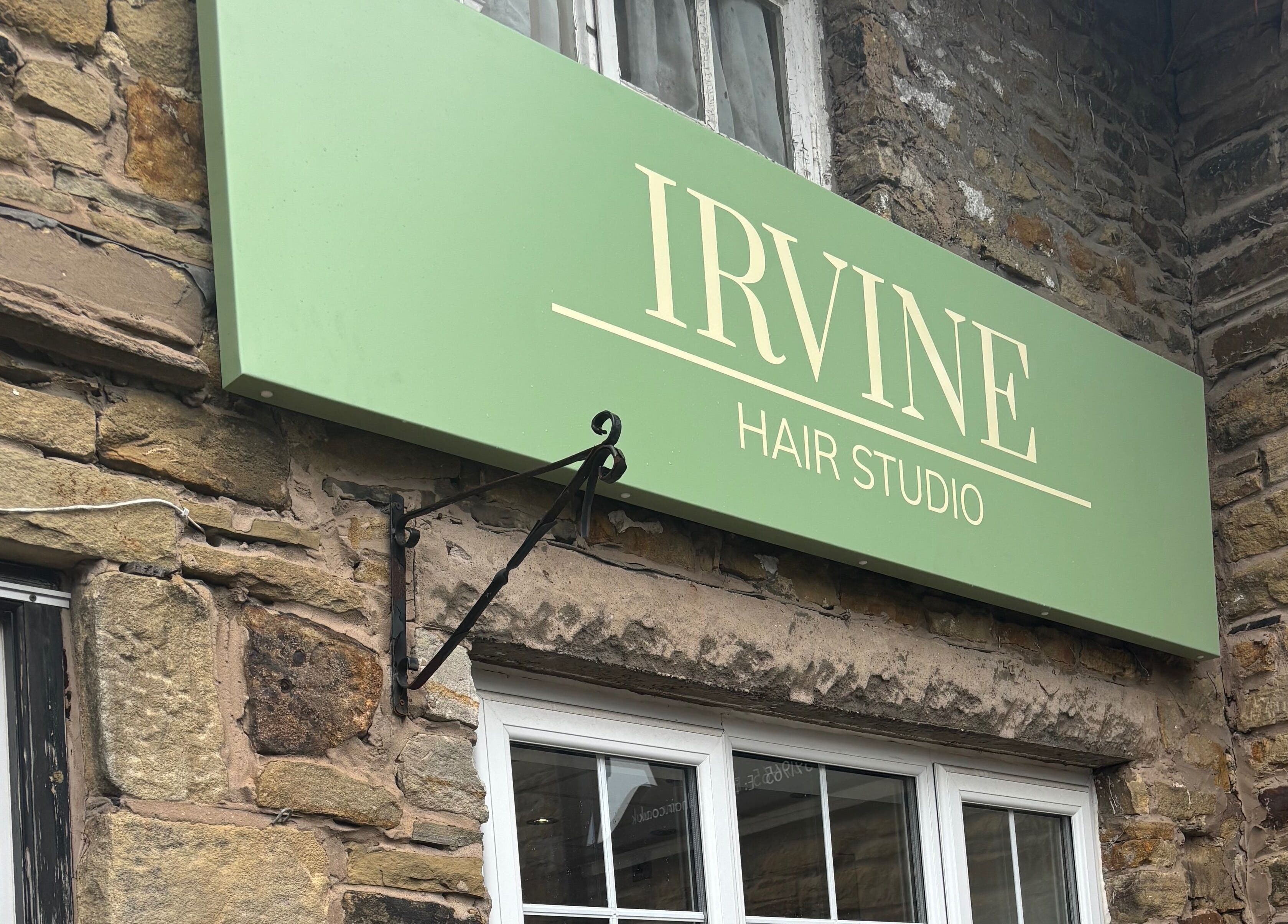 Elegant green sign of Irvine Hair Studio in Bolton, England, GB on a rustic stone wall.