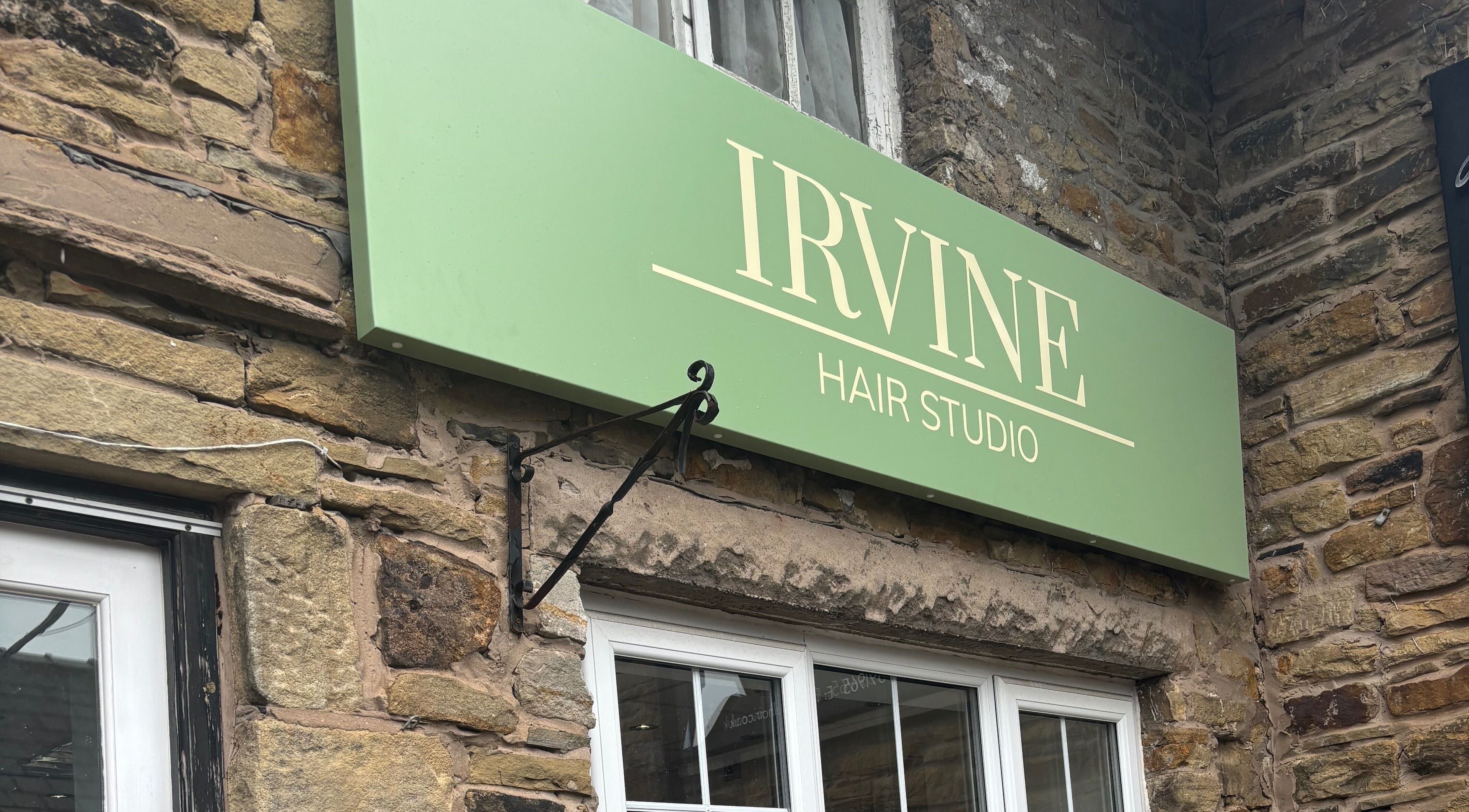 Elegant green sign of Irvine Hair Studio in Bolton, England, GB on a rustic stone wall.