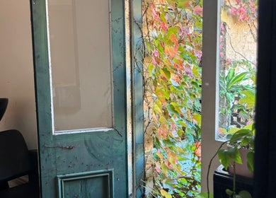 Lush green and pink leaves frame an open door at Hearth Hair, Wollongong, New South Wales, AU.
