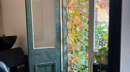 Lush green and pink leaves frame an open door at Hearth Hair, Wollongong, New South Wales, AU.