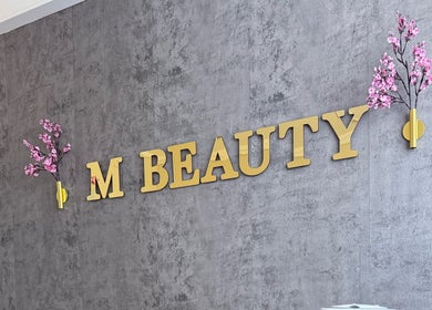 Elegant skilt på M Beauty i Skedsmokorset, Akershus, NO med blomsterdekorasjon på veggen.