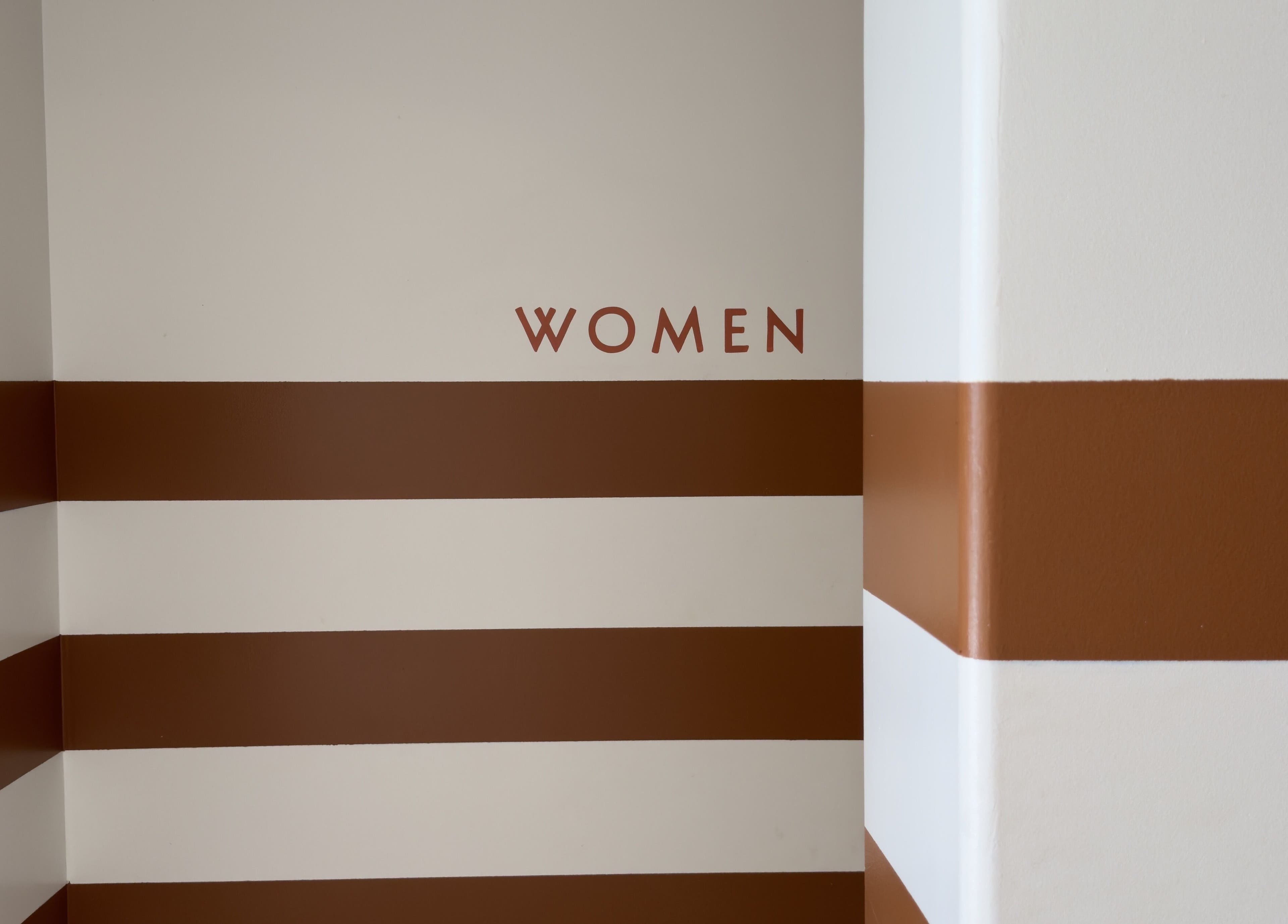 Mur rayé brun et blanc à LASH LOUNGE, Cenon, Nouvelle-aquitaine, FR avec inscription 'WOMEN'.