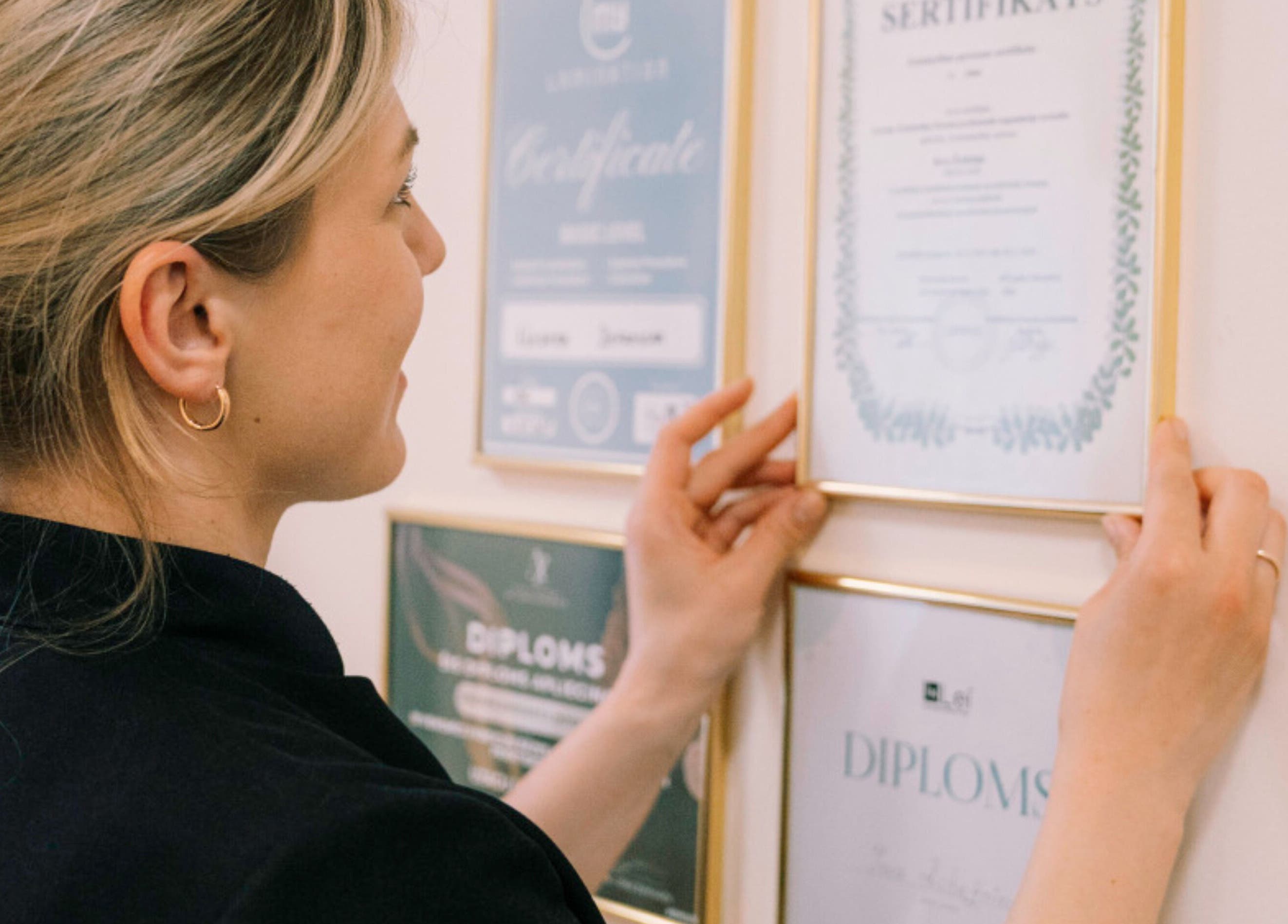 Woman arranging certificates on wall at Ernestīnes Iela 24 / Rīga, Āgenskalns, Rīga, LV.