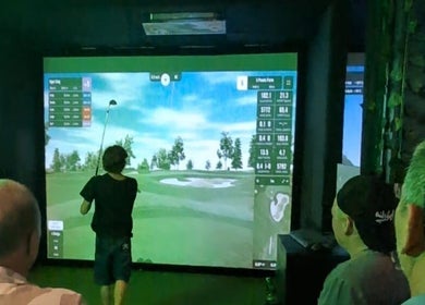 Guests enjoy a virtual golf game at The 19th Hole, Bali, Bali, ID on a large screen.