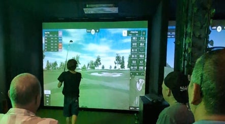 Guests enjoy a virtual golf game at The 19th Hole, Bali, Bali, ID on a large screen.