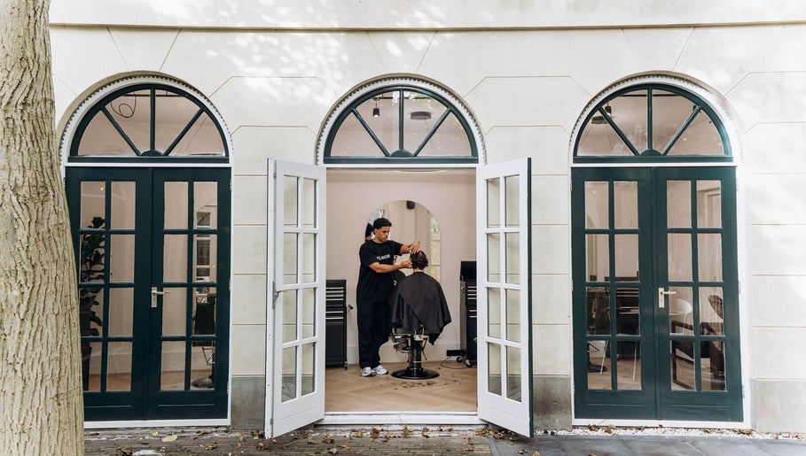 Kapper aan het werk bij CTDthelabel in Oosterhout, Noord-brabant, NL, gezien door een open deur.