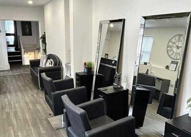 Modern salon interior at Glammedbyamelia in Plymouth, England, GB, showcasing sleek black chairs and large mirrors.