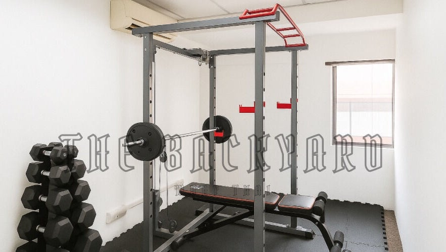 Gym setup at The Backyard Muay Thai in Kuala Lumpur, featuring weights and a workout bench.