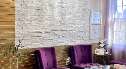 Elegant seating area at Mantra Thai Massage & Spa, Vienna, Virginia, US with purple chairs and white stone wall.