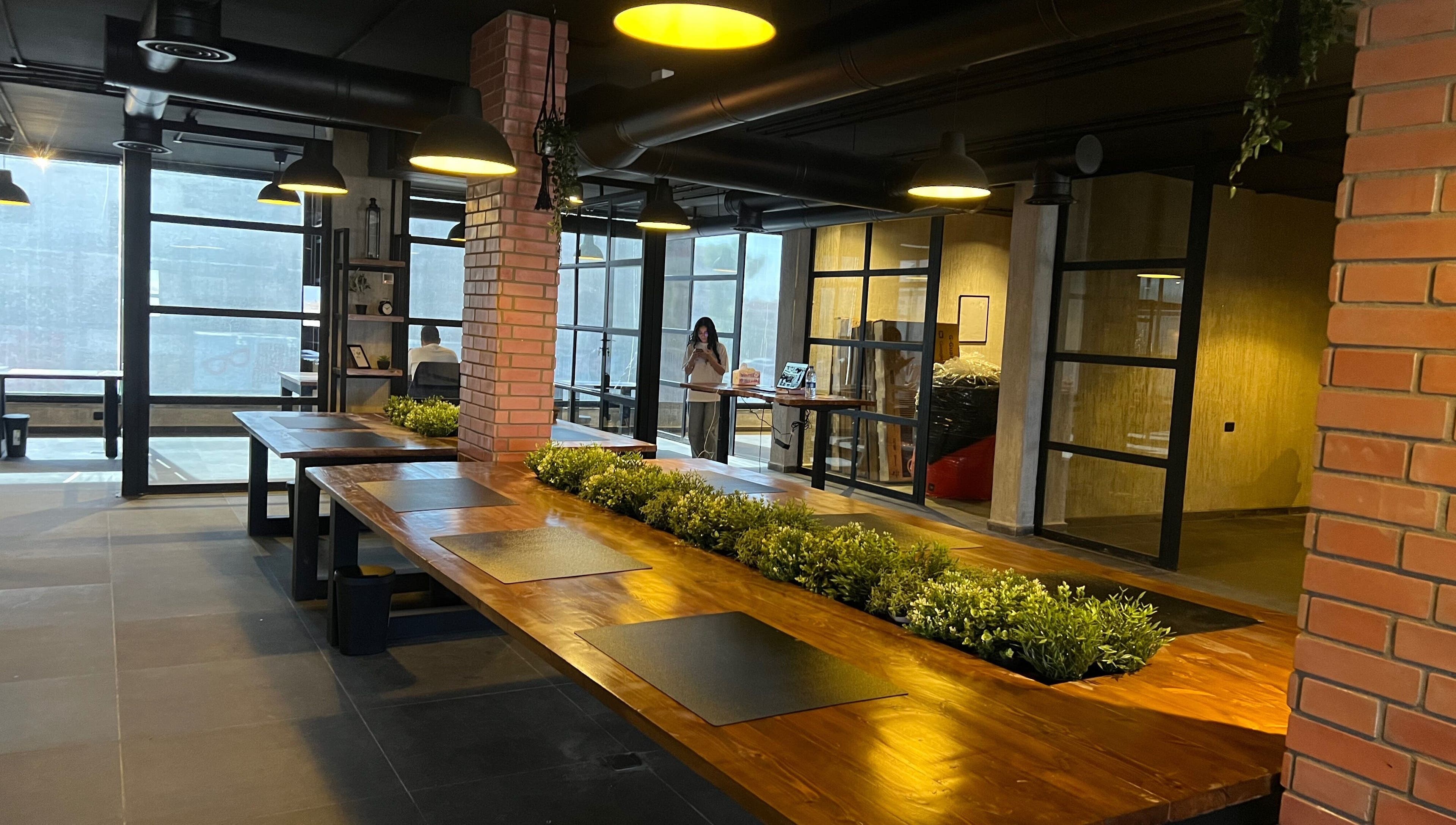 Spacious interior of Spaces offices, Az-zarqa, Zarqa Governorate, JO, featuring wooden tables and greenery.