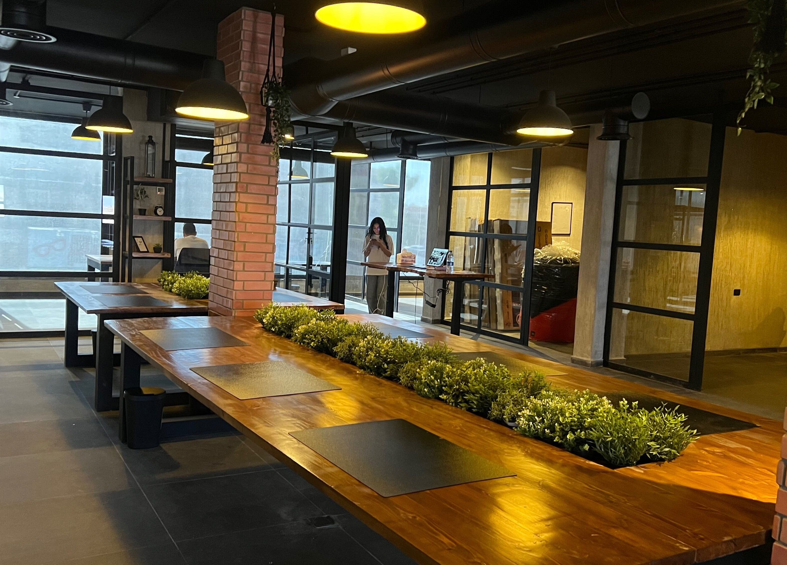 Spacious interior of Spaces offices, Az-zarqa, Zarqa Governorate, JO, featuring wooden tables and greenery.