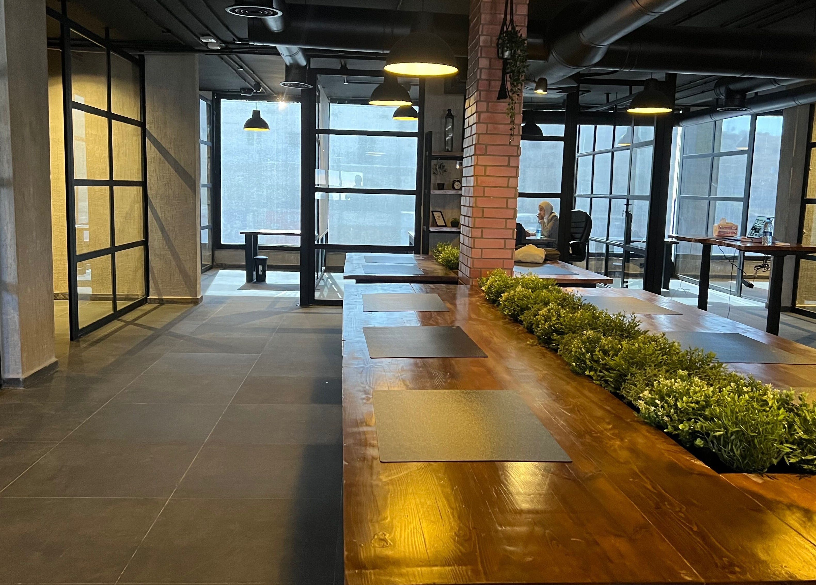 Modern workspace at Spaces offices, Az-zarqa, Zarqa Governorate, JO, featuring wooden tables and greenery.