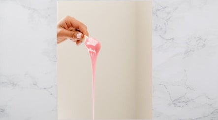 Hand holding pink wax at The OG Brazilianaire Studio in Spanish Fork, Utah, US, showcasing waxing services.